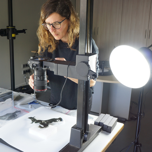 appareil photo fixé à un pied et positionné au-dessus de l'objet. Rebecca Perruche vérifie le rendu penchée sur l'appareil
